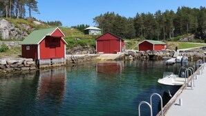 A calm waterfront with red buildings, clear water, and a dock with boats.