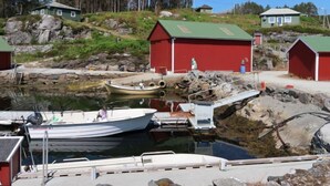 A harbor with boats docked, red buildings, and a rocky shoreline.
