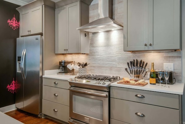 A modern kitchen with stainless steel appliances, grey cabinetry, and a countertop with a gas stove, wine glasses, and a bottle of champagne.