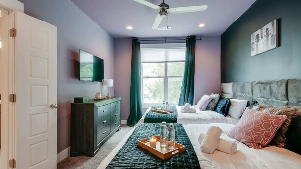 A bedroom with a bed, bedside tables, a dresser, a ceiling fan, a window with curtains, and a wall-mounted TV. - Nashville getaway: happy hour bar, disco theme room, bunk room, sleeps 12 (Nashville)