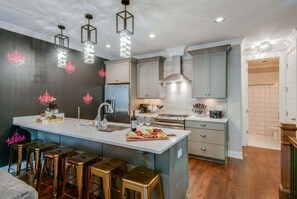 A modern kitchen with a central island, bar stools, stainless steel appliances, and pendant lighting.