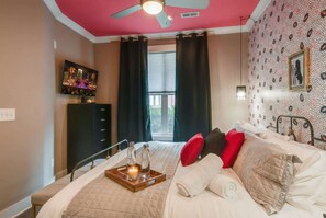 Una habitación de hotel con cama, televisor, ventilador de techo y ventana con cortinas.