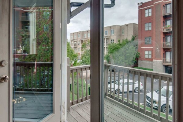 A view from a balcony with a wooden deck, overlooking a parking area and multi-story buildings.