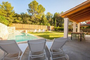 A backyard with a swimming pool, lounge chairs, and a covered patio area.