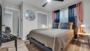 A bedroom with a bed, a desk, a chair, a ceiling fan, and a window with curtains.