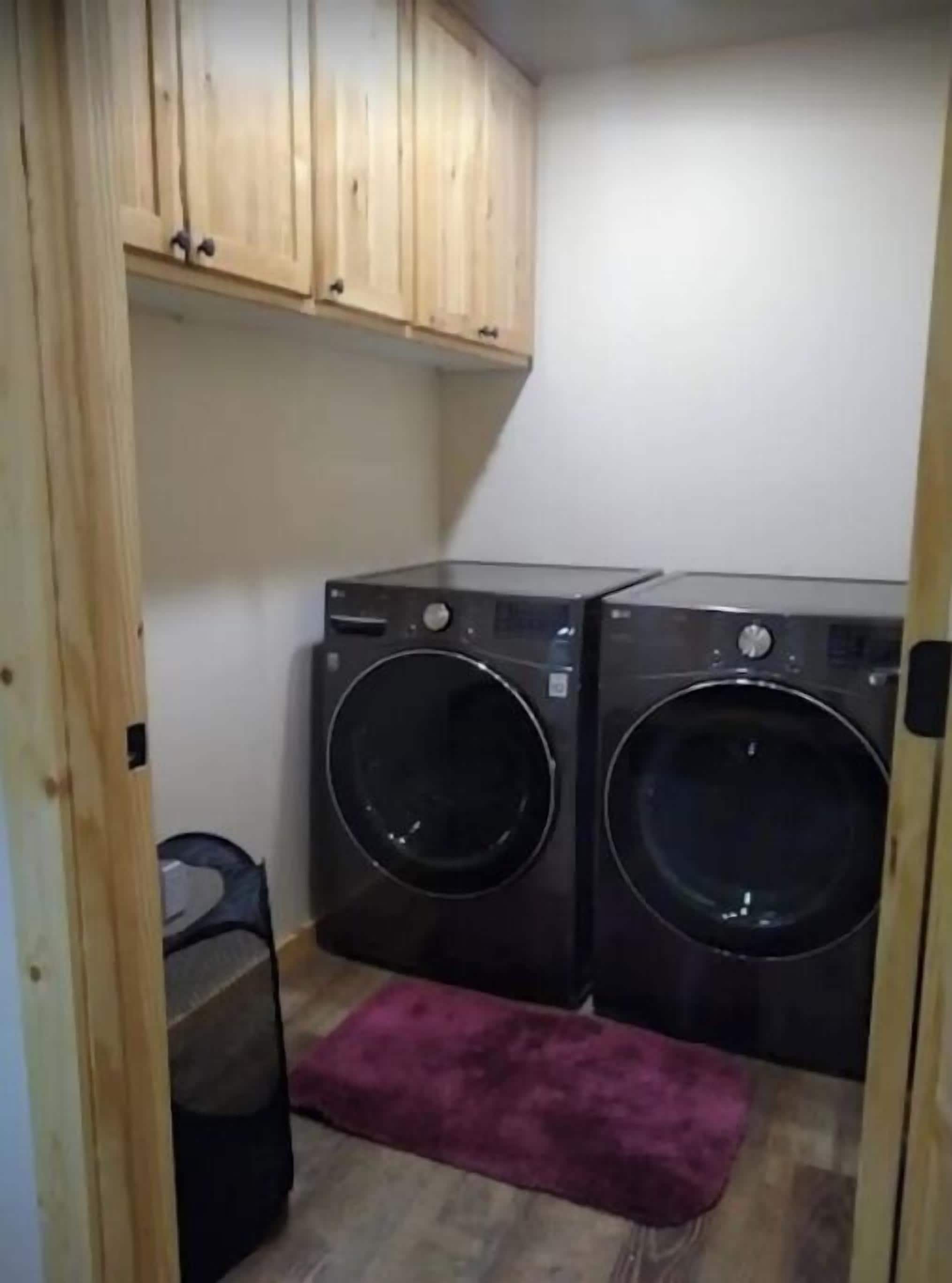 Ein Waschraum mit zwei schwarzen Waschmaschinen, Holzausstattung darüber und einer violetten Fußmatte.