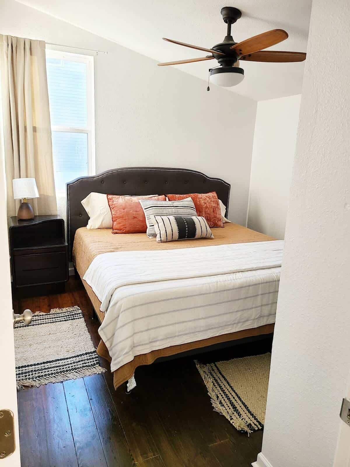 A bedroom with a bed, a nightstand, a lamp, a ceiling fan, and a window with curtains.