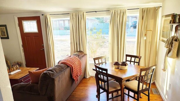 A cozy living room with a sofa, a dining table with chairs, and a wooden floor. - Cape Town Cottage 3 Blocks From Oaklawn (Hot Springs)