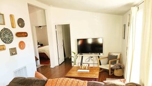 A living room with a TV, sofa, and coffee table. There are decorative plates on the wall and a plant on the table. - Cape Town Cottage 3 Blocks From Oaklawn (Hot Springs)