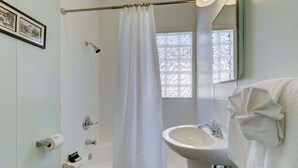 Une salle de bain équipée d’une baignoire, d’un lavabo, d’un rideau de douche, de toilettes et d’une fenêtre donnant sur les arbres.