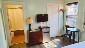A room with a bed, a desk with a lamp, a television, a chair, and a window with blinds. - Unit 15 King Bedroom, Mini Fridge, Wifi, Coffee Ma (Hot Springs)