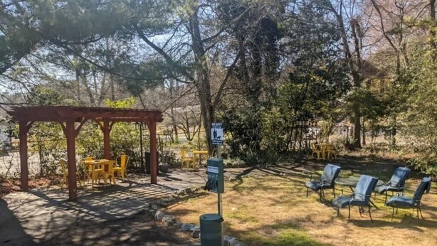 A covered seating area with chairs and a pergola, surrounded by trees and a grassy area. - Unit 15 King Bedroom, Mini Fridge, Wifi, Coffee Ma (Hot Springs)
