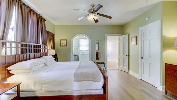 A bedroom with a wooden bed, a ceiling fan, and a view of a hallway with doors. - Unit 14 Roomy King Suite With Daybed Kitchenette, (Hot Springs)