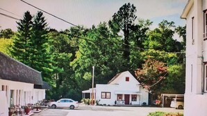 A quiet street with a white building, a parked car, and trees in the background. - Unit 14 Roomy King Suite With Daybed Kitchenette, (Hot Springs)
