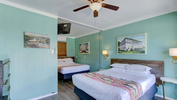 A hotel room with two beds, a ceiling fan, and artwork on the walls.