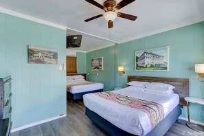 A hotel room with two beds, a ceiling fan, and artwork on the walls.