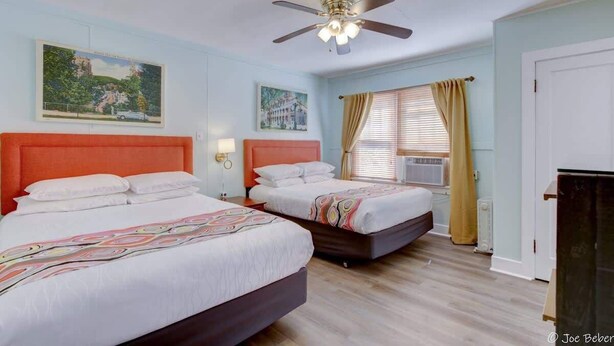 Une chambre d’hôtel avec deux lits, un ventilateur de plafond et des œuvres d’art accrochées aux murs.