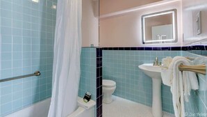 Ein Badezimmer mit blauen und weißen Fliesen, einer weißen Badewanne, einer weißen Toilette, einem Waschbecken mit Spiegel und einem Handtuchhalter.