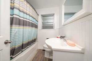 A bathroom with a striped shower curtain, a toilet, a sink with a soap dish, and a window above the sink.