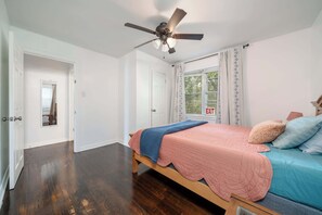 A bedroom with a bed, a ceiling fan, a window with curtains, and an exit sign.