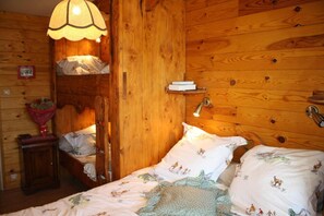 Um quarto de madeira acolhedor, com uma cama, uma mesa de cabeceira, um abajur e uma estante com livros.