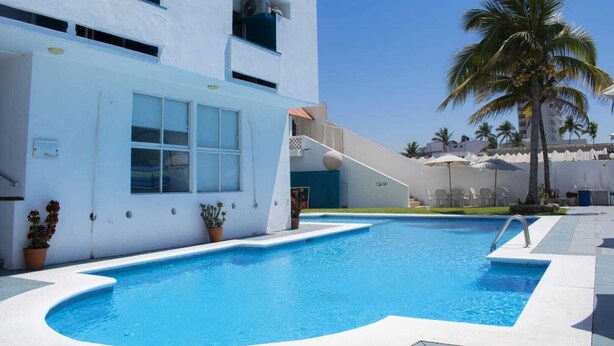 Una piscina con una decoración en blanco y azul, rodeada por un edificio blanco con balcones y plantas en macetas.