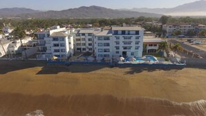 Un hotel frente al mar con varios pisos, piscina y una zona de playa arenosa.