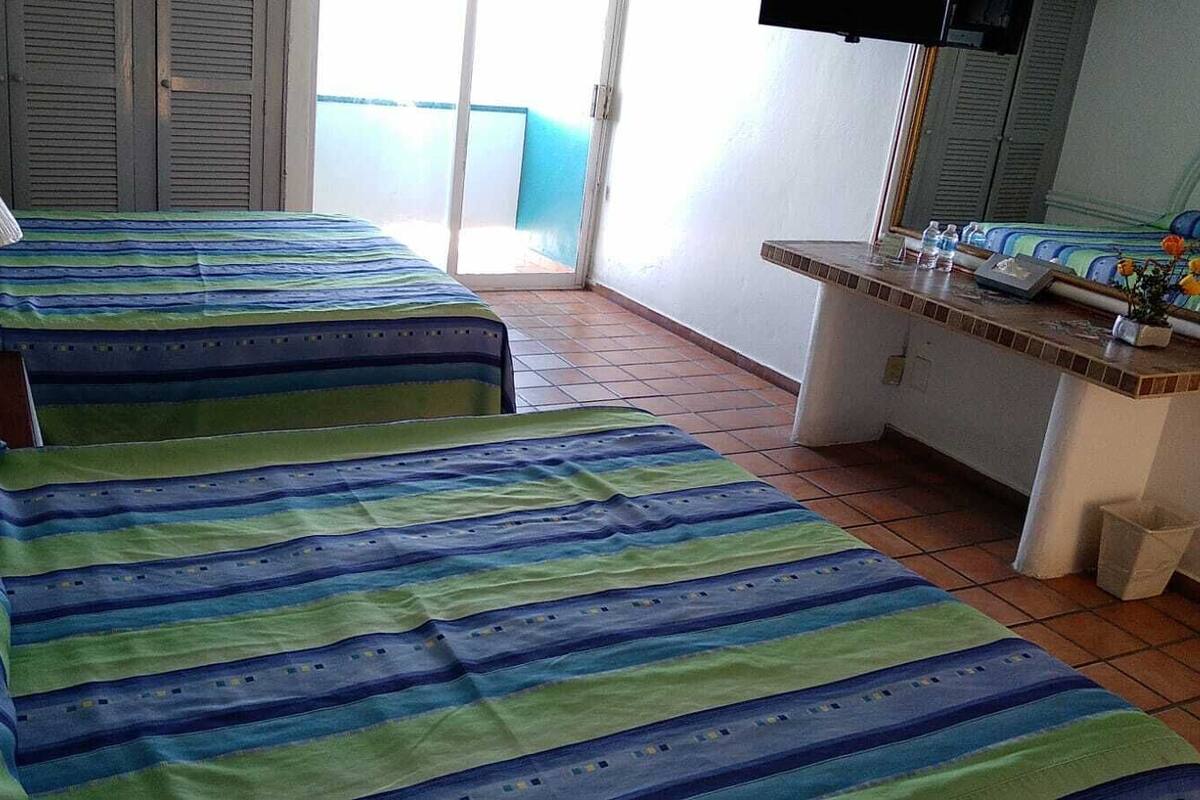 A room with two beds, a lamp, a small table with toiletries, and a window with a view.