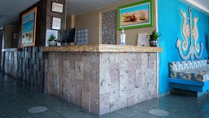 Un área de recepción con mostrador de piedra, obras de arte enmarcadas, pantalla digital y pared azul con decoración de ancla.
