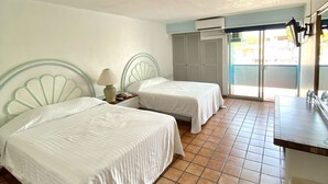 Habitación de hotel con dos camas, un escritorio pequeño, una silla, un ventanal con persianas y piso de baldosas.