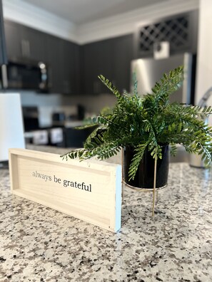 A sign of gratitude sits atop a granite countertop, accompanied by a potted fern.