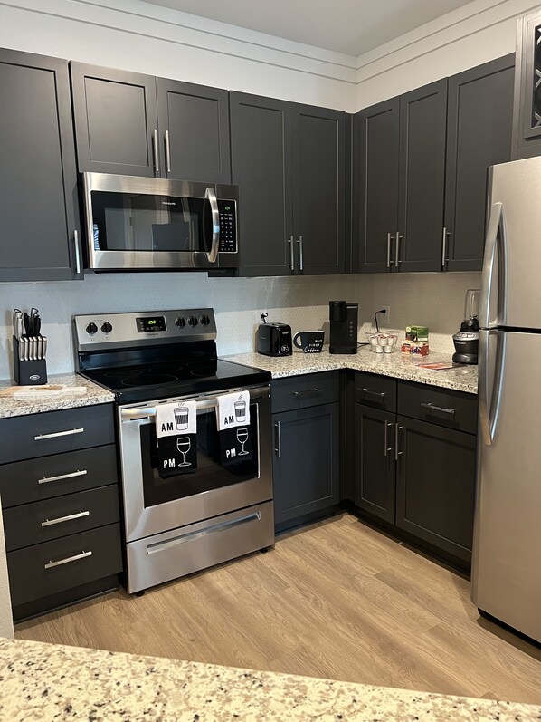 Features a kitchen with stainless steel appliances, dark cabinetry, and granite countertops.
