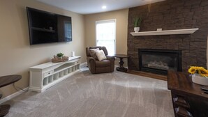 A living room with a stone fireplace, a ceiling fan, and a flat-screen TV mounted on the wall.