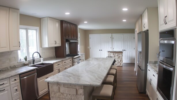 A spacious kitchen with white cabinets, a marble island, and stainless steel appliances.