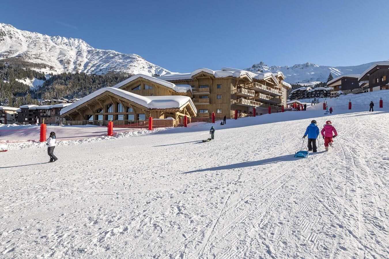 A ski resort with wooden buildings, a ski slope, and snow-covered mountains.