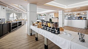 A spacious, modern kitchen area with a buffet setup, featuring a long table with various food containers and a counter with kitchen appliances.