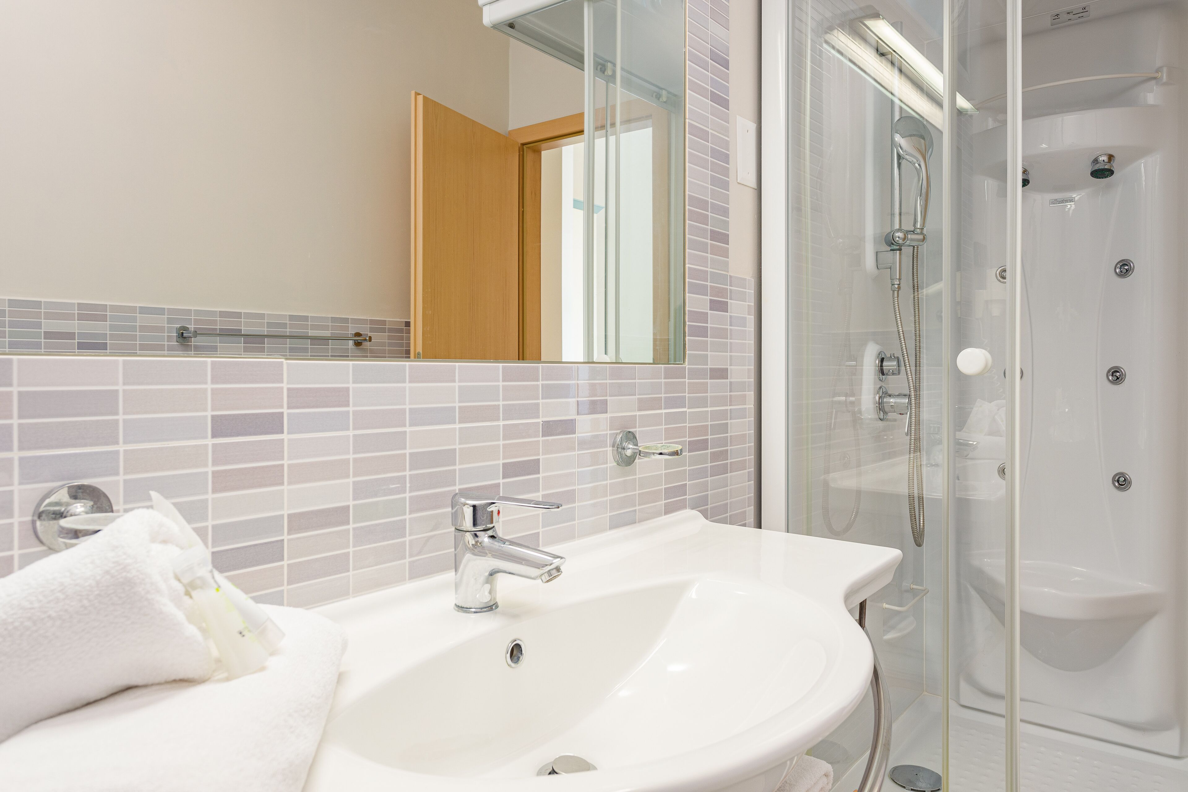 Un bagno con un lavandino bianco, una cabina doccia in vetro e uno specchio sopra il lavandino.