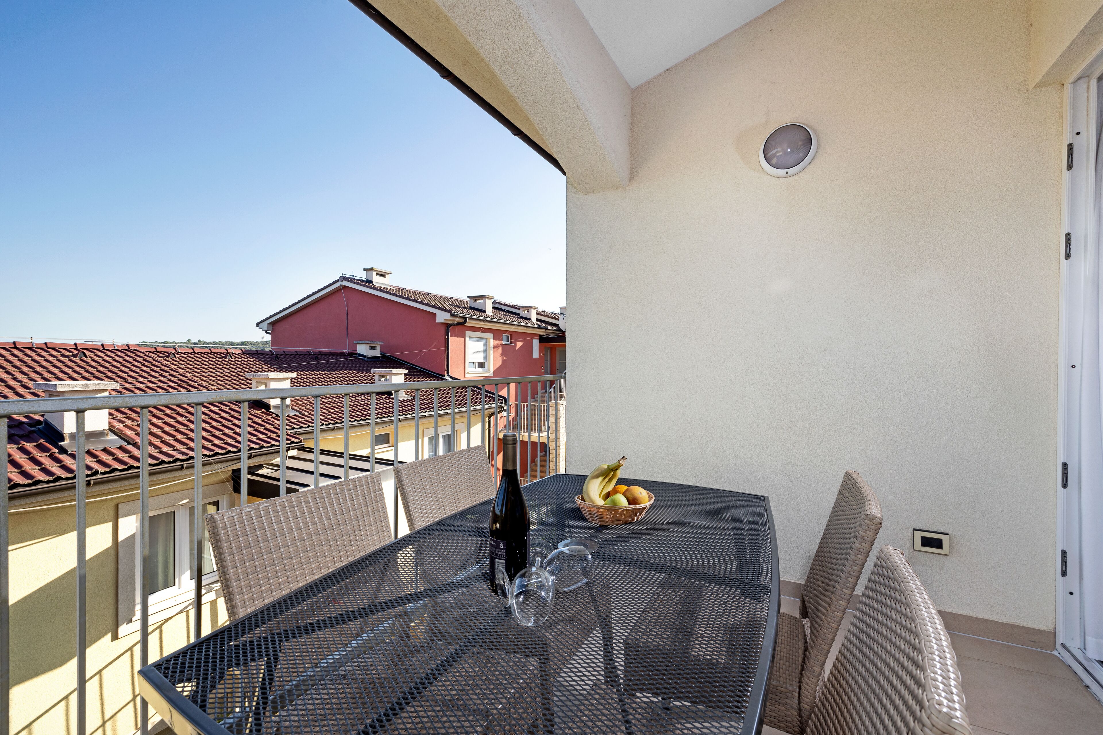Een balkon met een tafel, stoelen, een fles wijn en een fruitschaal.
