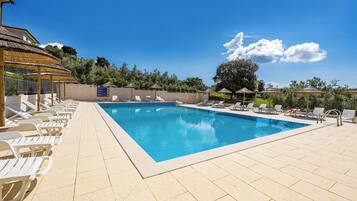 A swimming pool with lounge chairs and umbrellas, surrounded by a fence and trees.