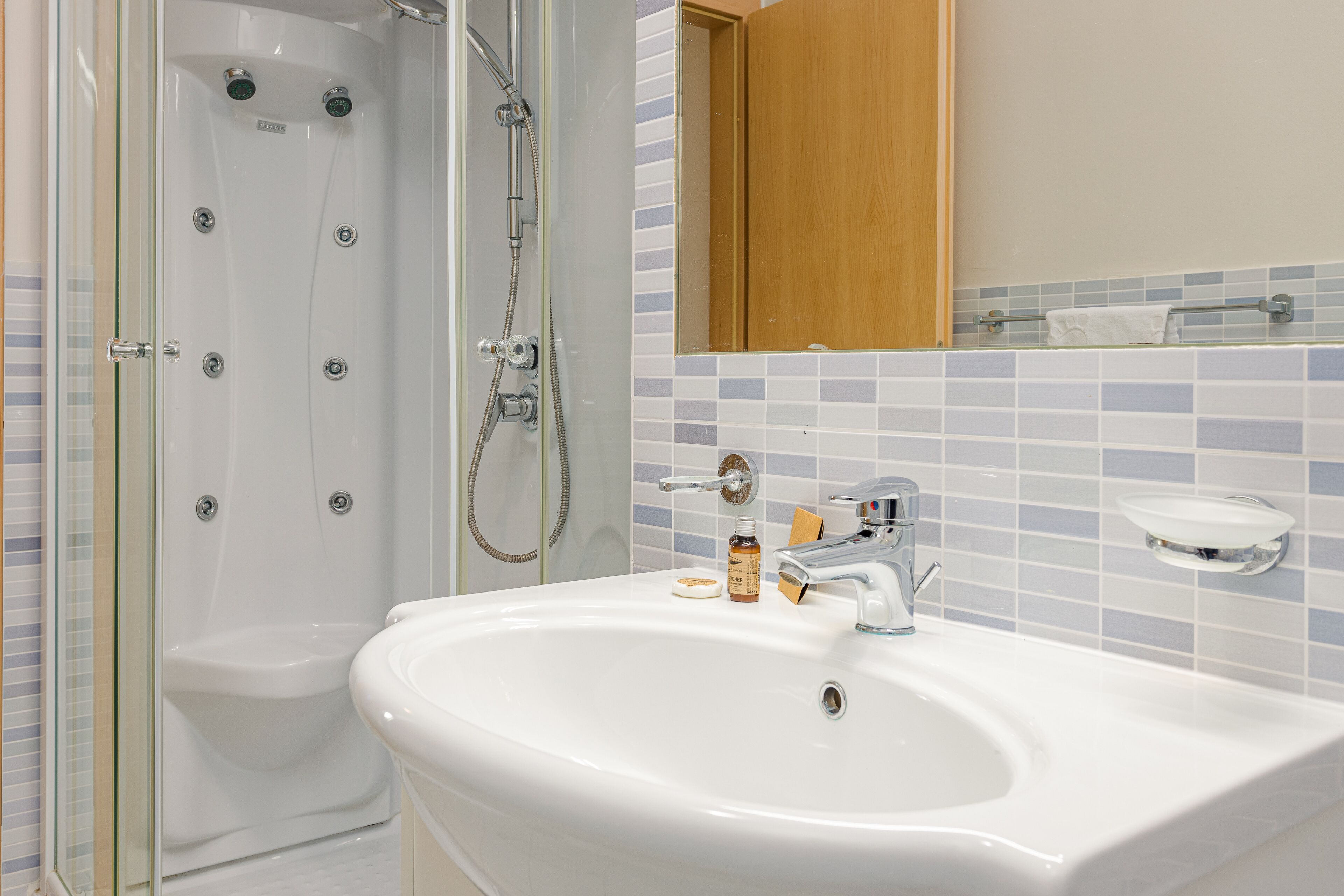 Une salle de bain avec une douche à parois de verre, un lavabo blanc doté d’un distributeur de savon et un miroir au-dessus du lavabo.