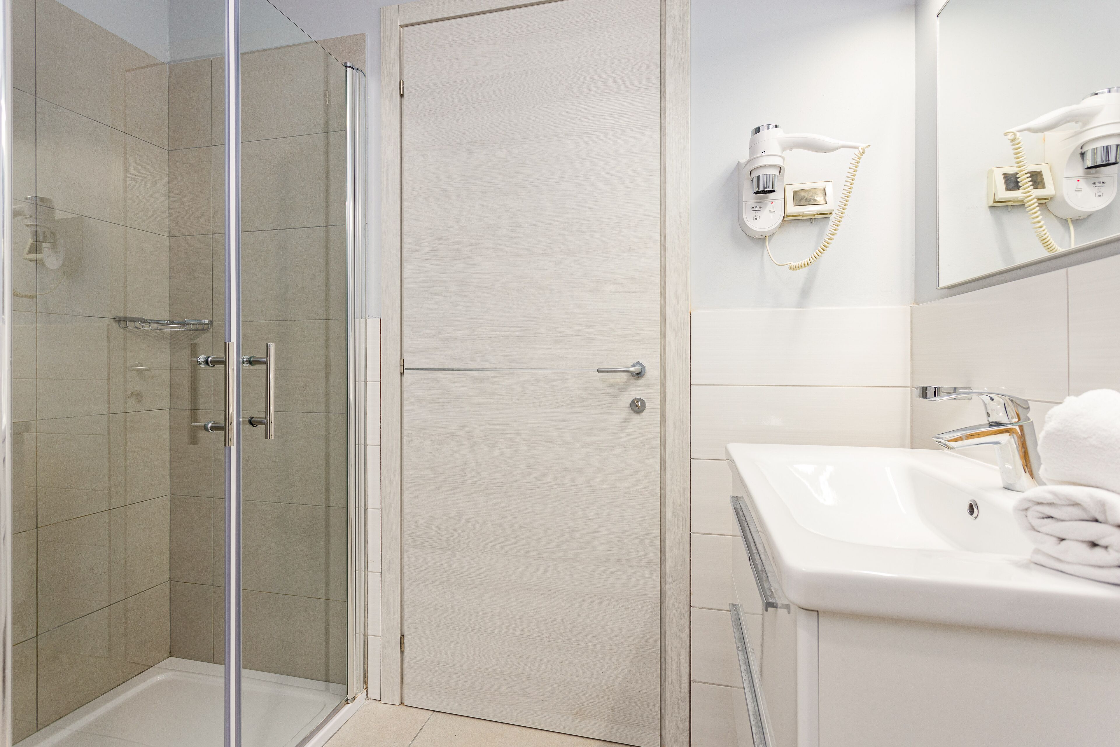 A modern bathroom with a glass shower enclosure, a white sink with a gold faucet, and a towel rack.