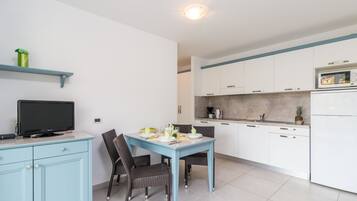 Een moderne keuken met witte kastjes, een blauwe eettafel en een flatscreen televisie op een lichtblauwe kast.