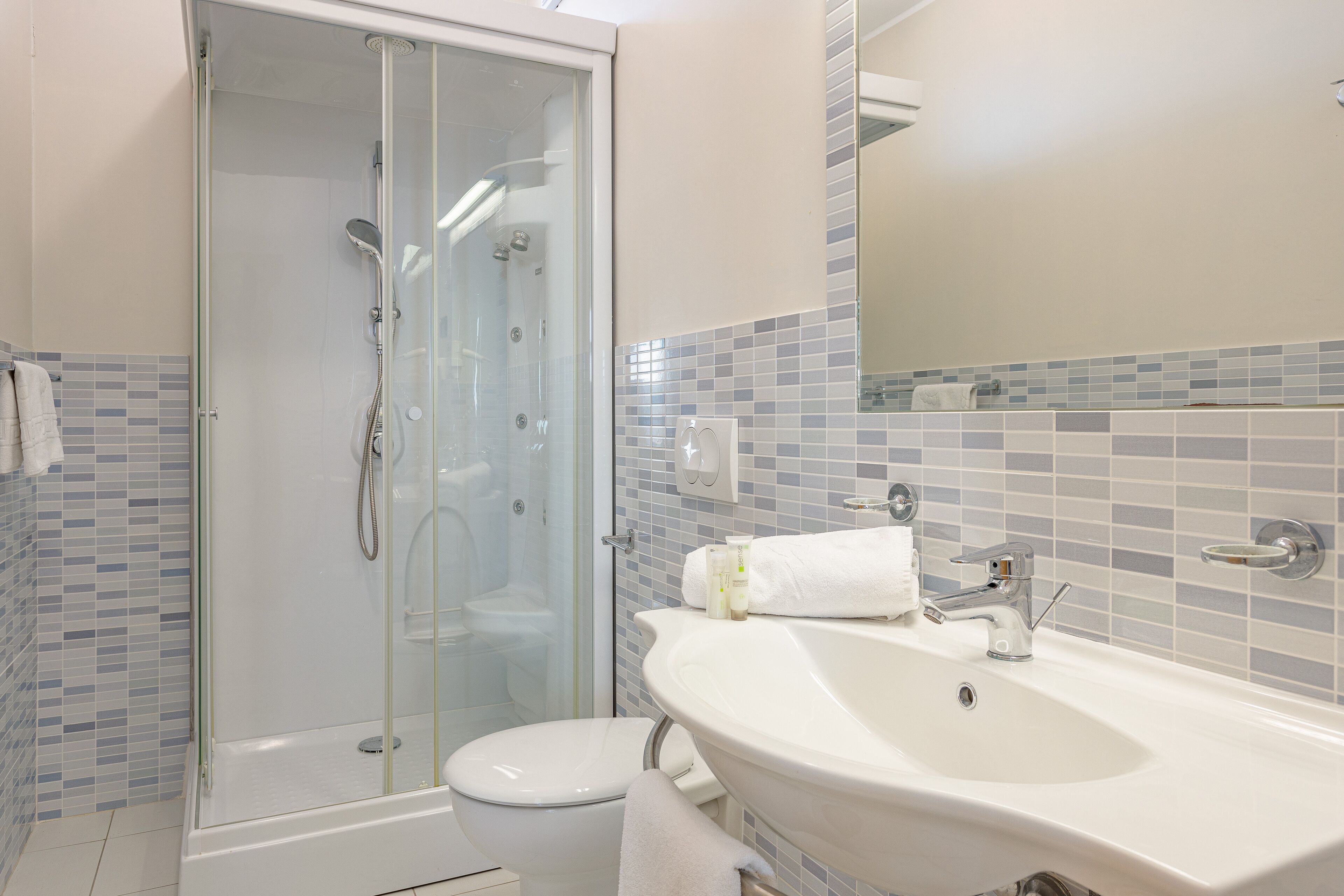 Une salle de bain avec une douche à parois de verre, un lavabo blanc et un mur recouvert de carreaux.