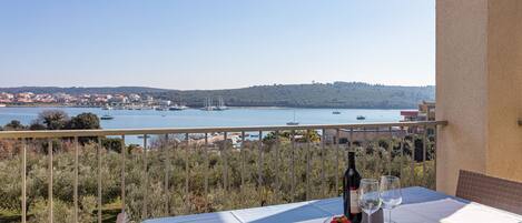 A balcony with a table set for two, overlooking a body of water with boats and a distant town.