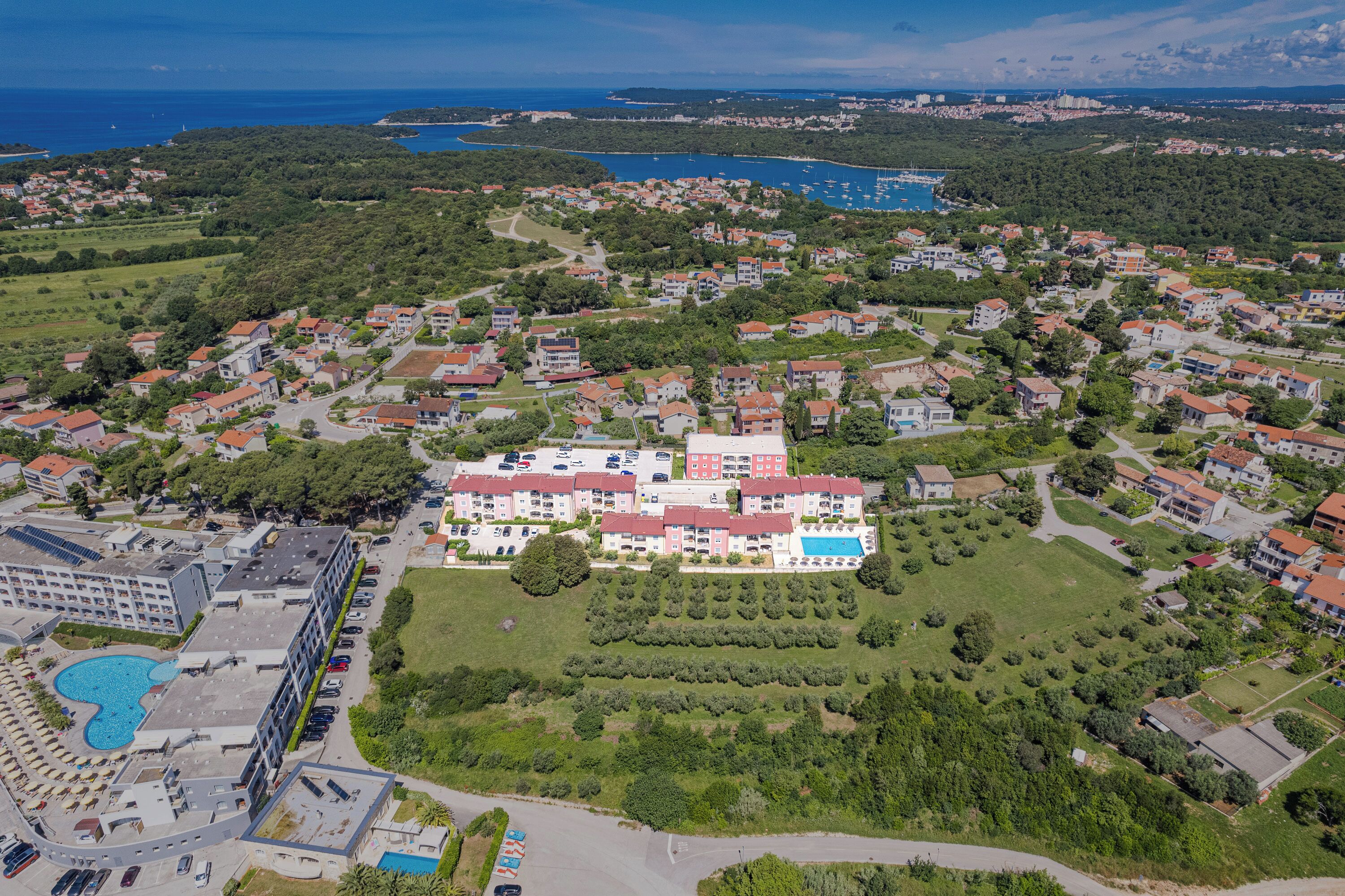 Vista aérea de un pueblo costero con un hotel destacado que cuenta con varios pisos, una piscina y un jardín bien cuidado.