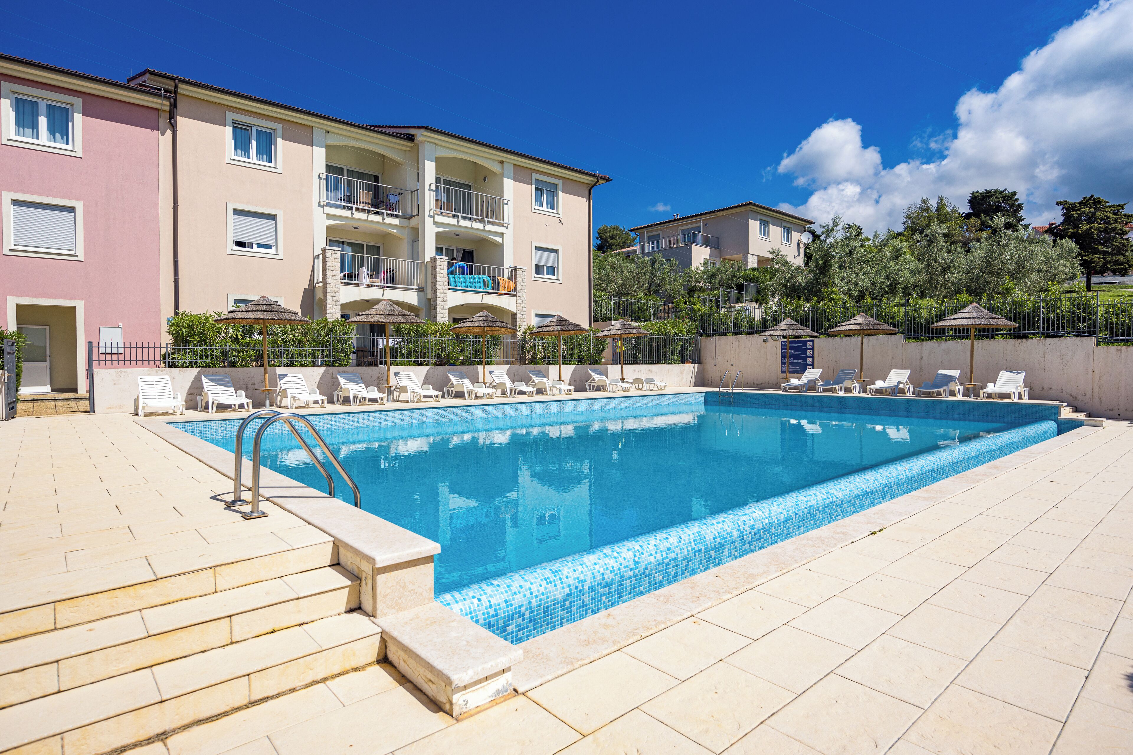 A swimming pool with steps leading into it, surrounded by lounge chairs and umbrellas.