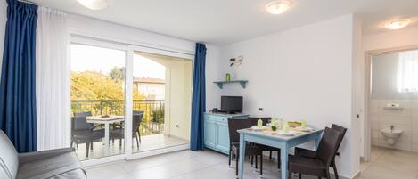A modern apartment with a balcony, a dining area, a sofa, and a kitchenette.