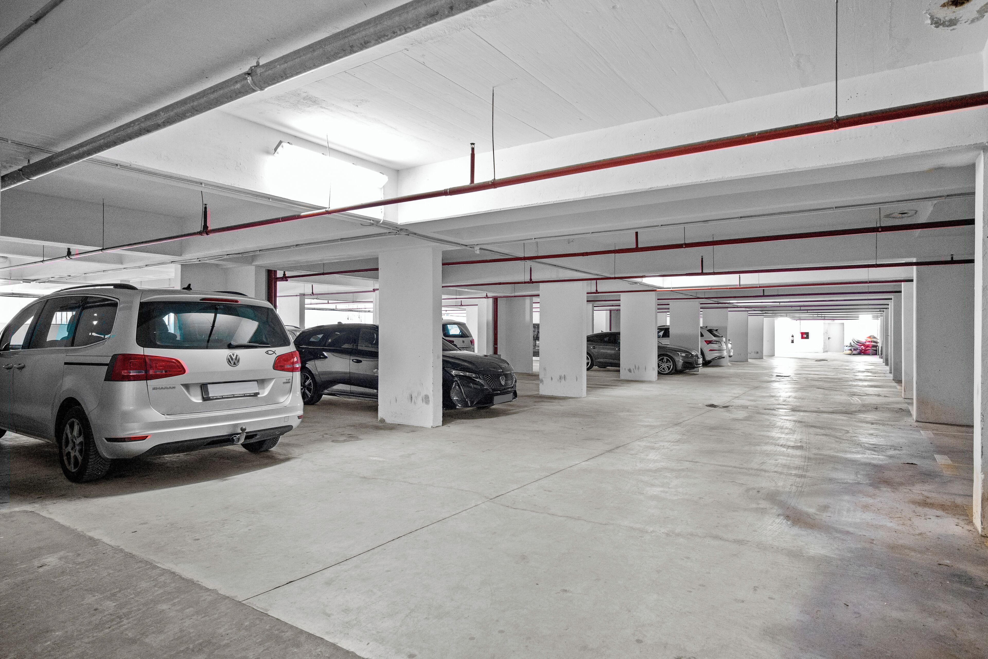 Useita kerroksia sisältävä pysäköintihalli, jossa on betonipilarit ja katossa kulkevat putket.