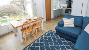 A modern kitchen with white cabinets, a black range hood, and a dining area with a wooden table and chairs. - Chalfonts Cottage (Haverfordwest)