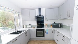 A modern kitchen with white cabinets, a black stove, and a window overlooking greenery. - Chalfonts Cottage (Haverfordwest)